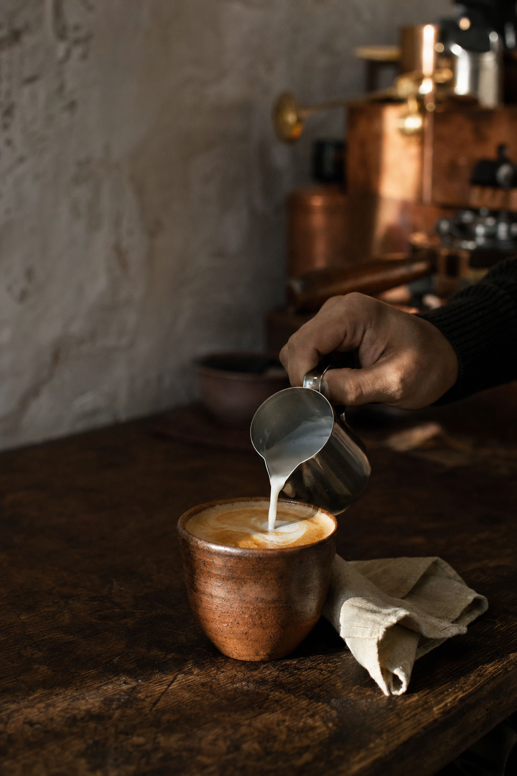 A barista finishing a cappuccino in a handmade ceramic cup
